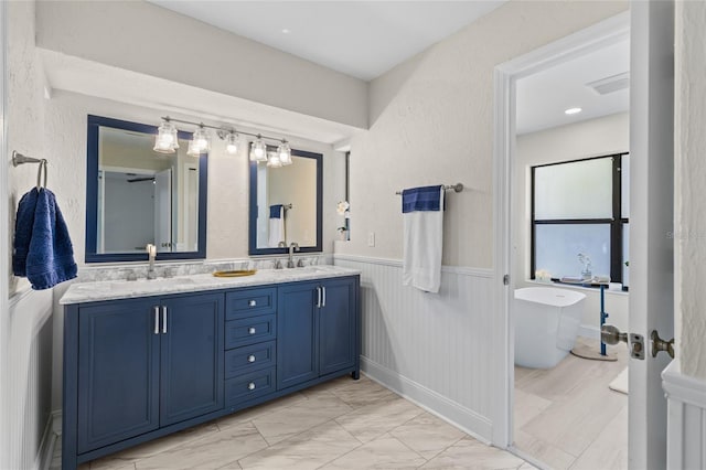 bathroom with a wainscoted wall, marble finish floor, a sink, double vanity, and a soaking tub