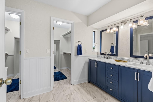 bathroom featuring double vanity, wainscoting, marble finish floor, and a sink