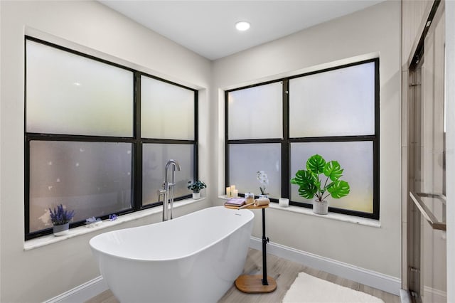 bathroom with recessed lighting, baseboards, a soaking tub, and wood finished floors