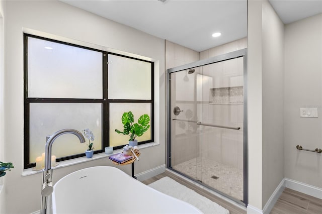 bathroom featuring a stall shower, a freestanding bath, baseboards, and wood finished floors