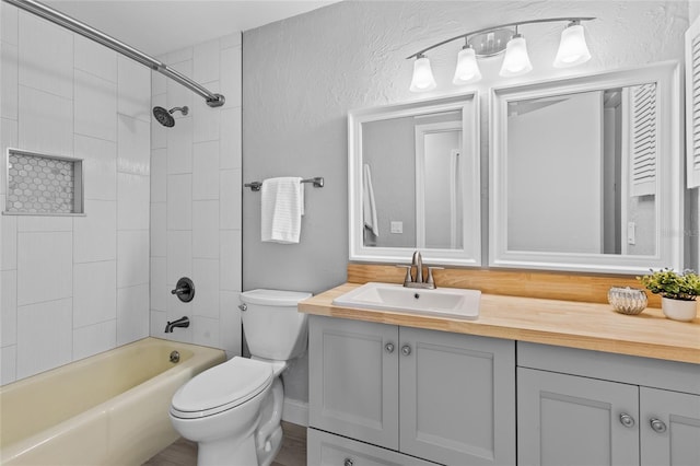 bathroom with toilet, vanity, shower / bathing tub combination, and a textured wall