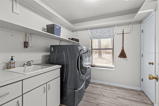 laundry area featuring washing machine and clothes dryer, baseboards, light wood-type flooring, cabinet space, and a sink