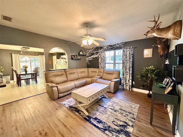 living area with arched walkways, visible vents, ceiling fan, and wood finished floors