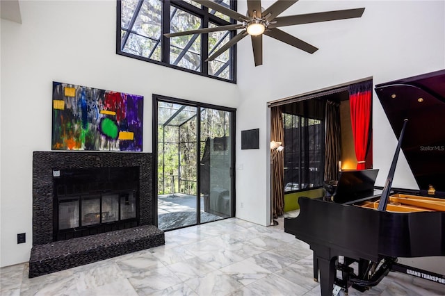 living area with a glass covered fireplace, a high ceiling, marble finish floor, and ceiling fan