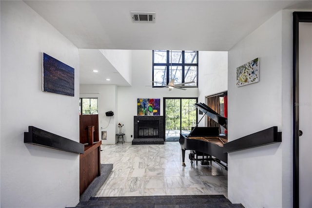 foyer with visible vents, a towering ceiling, a glass covered fireplace, marble finish floor, and a ceiling fan