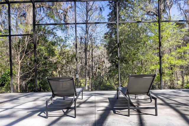 view of patio / terrace featuring a lanai and a wooded view