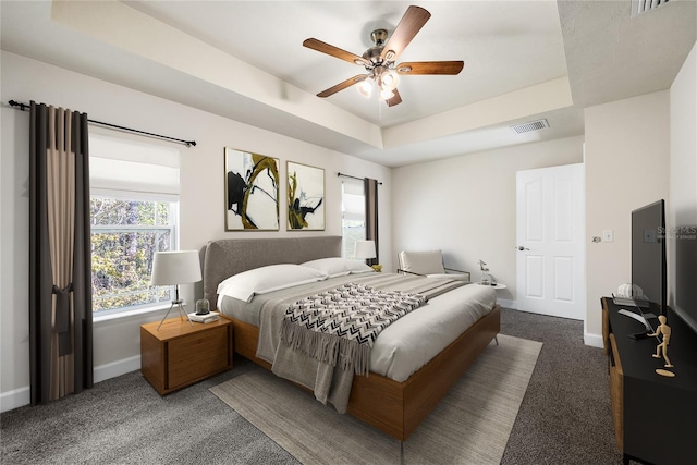 carpeted bedroom with a tray ceiling, baseboards, visible vents, and ceiling fan