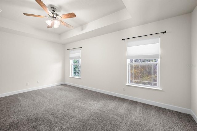 carpeted spare room with baseboards, a raised ceiling, and a ceiling fan