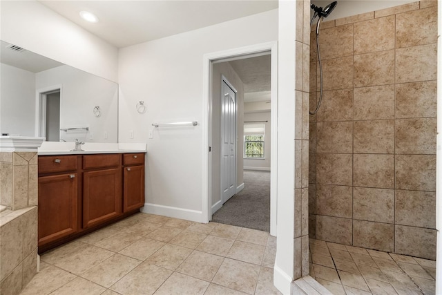 bathroom with tile patterned flooring, visible vents, baseboards, tiled shower, and vanity