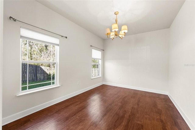 empty room with baseboards, an inviting chandelier, and dark wood finished floors