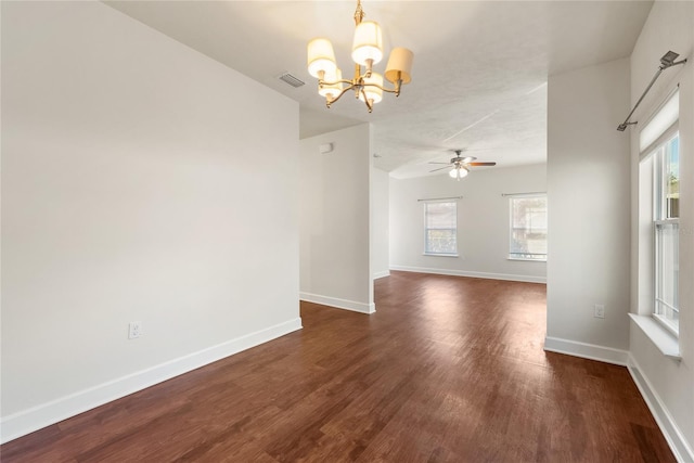 spare room with ceiling fan with notable chandelier, dark wood-style floors, visible vents, and baseboards