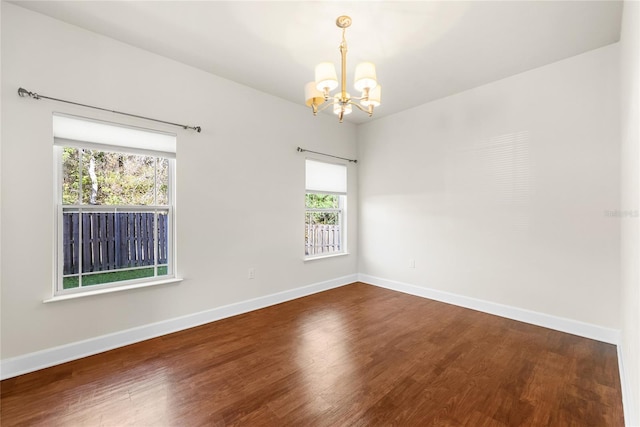 unfurnished room with baseboards, wood finished floors, and a chandelier