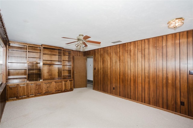 unfurnished living room featuring light colored carpet, visible vents, wood walls, and ceiling fan