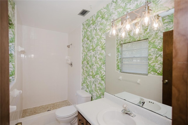 bathroom with a notable chandelier, toilet, wallpapered walls, tiled shower, and vanity