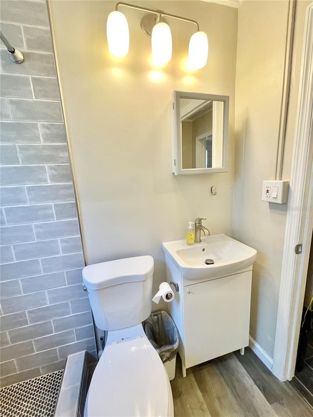 bathroom featuring vanity, toilet, wood finished floors, and a tile shower