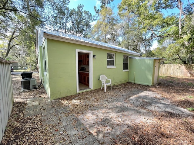 rear view of house featuring a patio, fence, concrete block siding, metal roof, and central AC unit