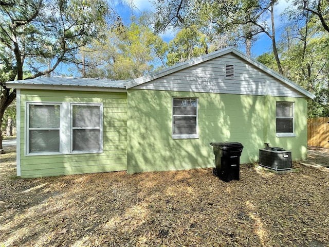 view of side of property with metal roof, central AC unit, concrete block siding, and fence