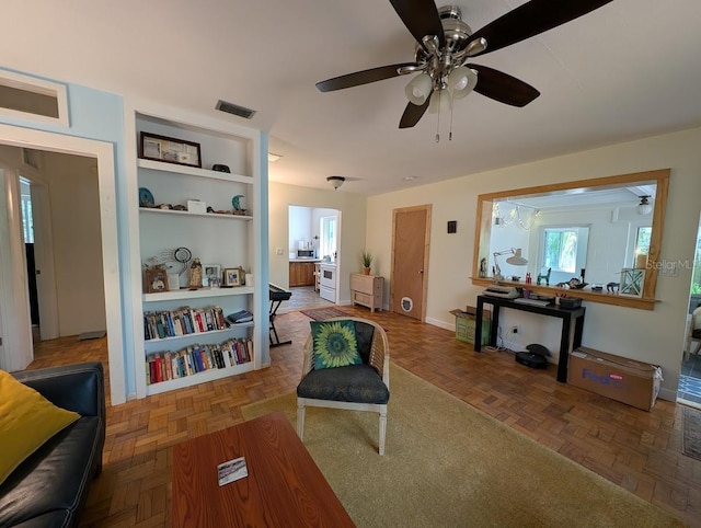 living room with built in shelves, visible vents, and ceiling fan