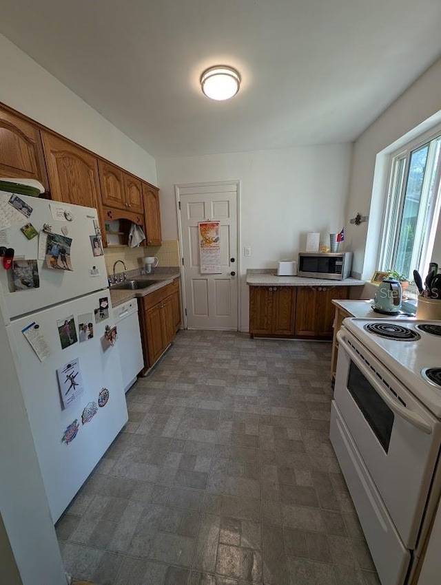 kitchen with white appliances, light countertops, brown cabinets, and a sink