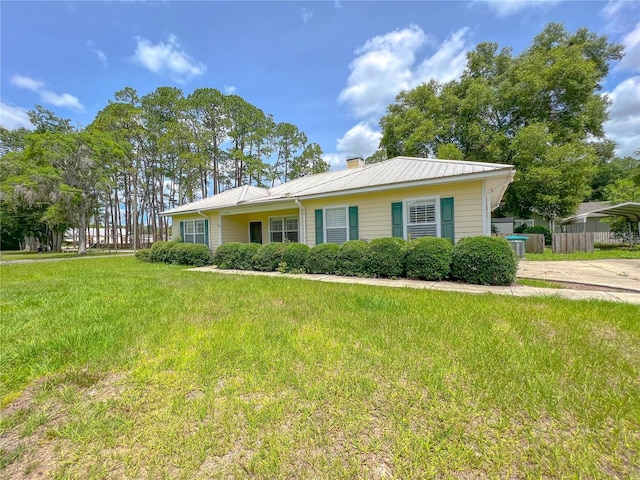 single story home featuring a front lawn, fence, a detached carport, metal roof, and a chimney