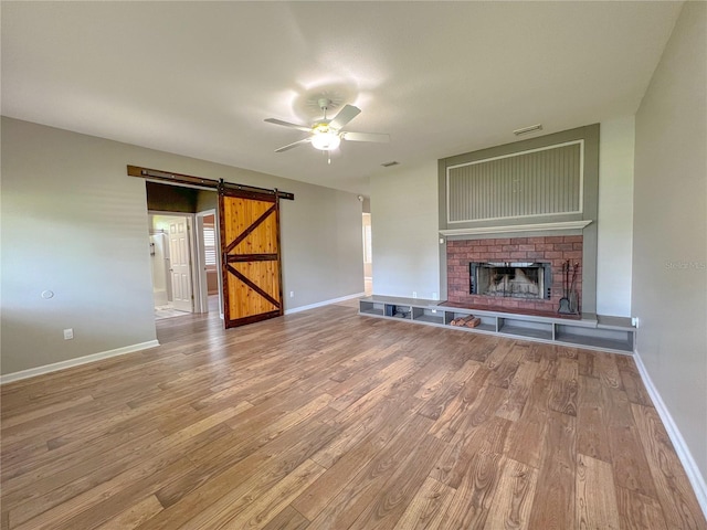 unfurnished living room featuring visible vents, wood finished floors, a barn door, a brick fireplace, and ceiling fan