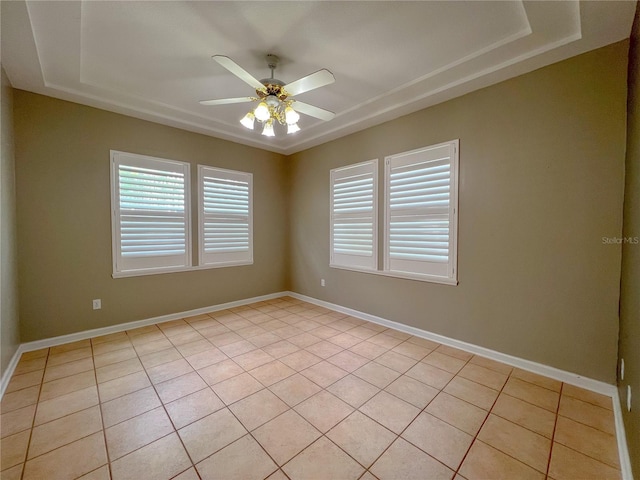 spare room with a tray ceiling, baseboards, a healthy amount of sunlight, and a ceiling fan