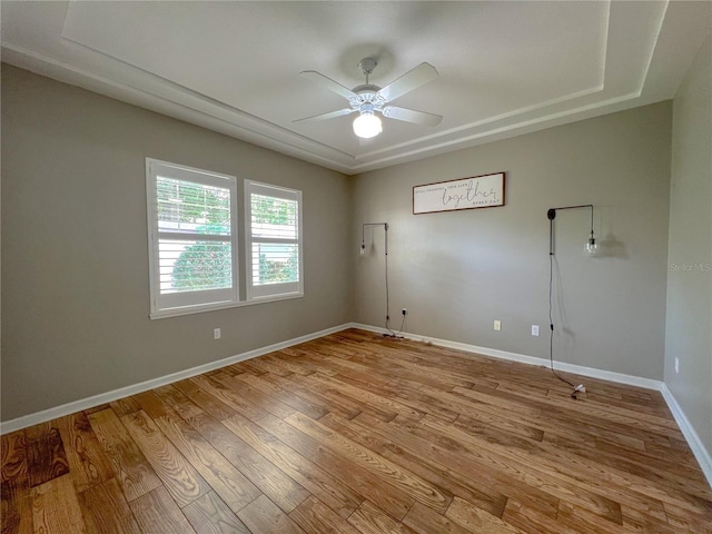 spare room featuring ceiling fan, baseboards, a raised ceiling, and light wood-style floors