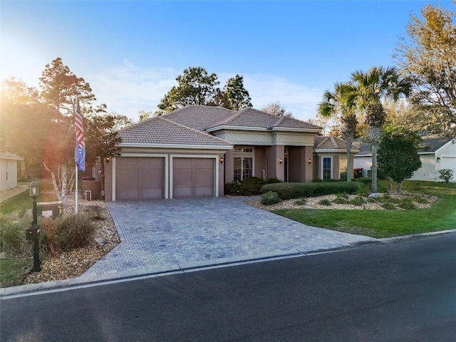 view of front of home featuring stucco siding, a tile roof, decorative driveway, and a garage