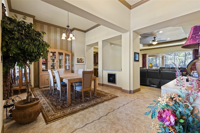 dining area featuring ceiling fan with notable chandelier, a tray ceiling, baseboards, and ornamental molding