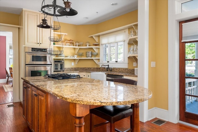 kitchen featuring light stone counters, visible vents, dark wood-style flooring, a sink, and stainless steel appliances