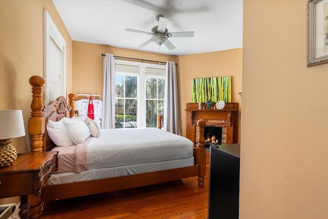 bedroom featuring a fireplace, a ceiling fan, and wood finished floors