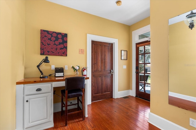 office with visible vents, baseboards, dark wood-style flooring, and built in desk