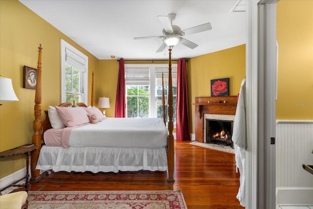 bedroom with visible vents, a fireplace with flush hearth, wood finished floors, and a ceiling fan
