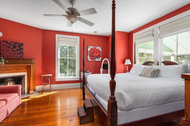 bedroom featuring baseboards, multiple windows, a fireplace with flush hearth, and hardwood / wood-style flooring