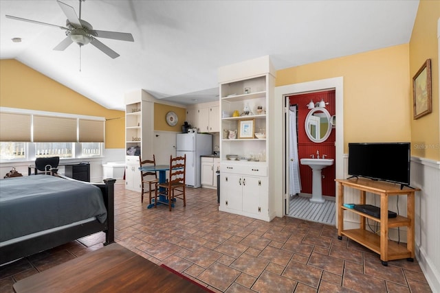 bedroom with wainscoting, freestanding refrigerator, lofted ceiling, and a sink