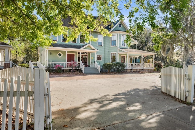 view of front of property with a gate, driveway, roof with shingles, covered porch, and a fenced front yard