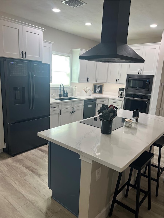 kitchen featuring a kitchen breakfast bar, island exhaust hood, a sink, white cabinetry, and black appliances