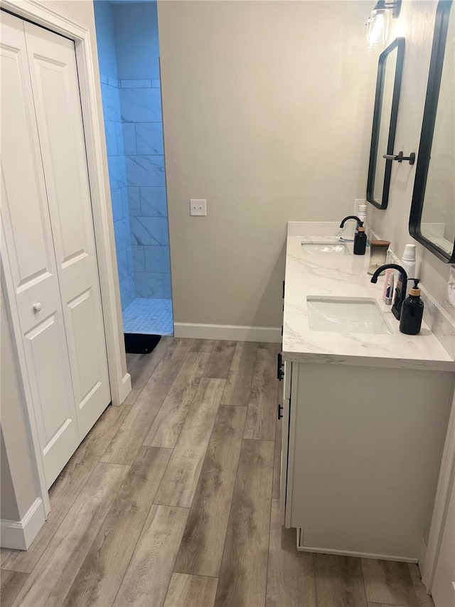 bathroom featuring baseboards, wood finished floors, a sink, and a tile shower