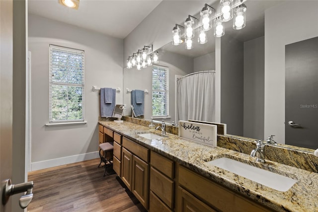 full bathroom featuring baseboards, double vanity, a sink, and wood finished floors