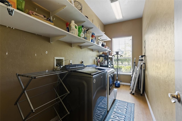 laundry area with laundry area, baseboards, washer and dryer, light wood-style floors, and a textured wall