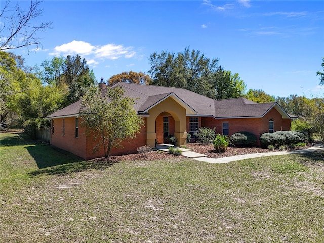 ranch-style house featuring a shingled roof, a chimney, a front yard, and stucco siding