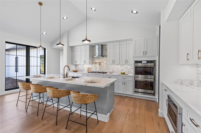 kitchen with a kitchen breakfast bar, a sink, appliances with stainless steel finishes, and wall chimney range hood