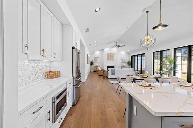 kitchen featuring open floor plan, vaulted ceiling, light wood-style floors, a fireplace, and appliances with stainless steel finishes