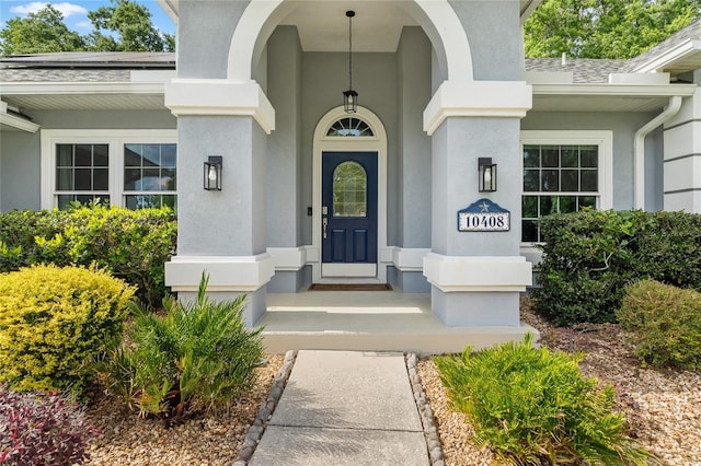doorway to property with roof with shingles, stucco siding, and roof mounted solar panels