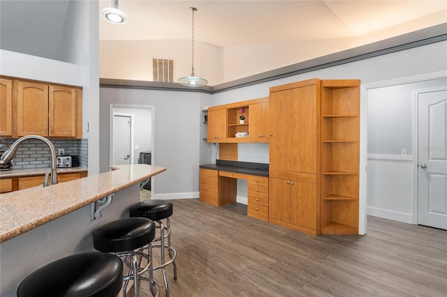kitchen with a breakfast bar, vaulted ceiling, built in study area, open shelves, and wood finished floors