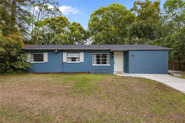 single story home featuring concrete block siding, a front yard, and driveway