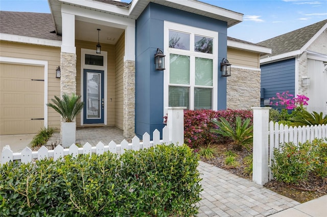 property entrance with stone siding, a garage, fence, and a shingled roof