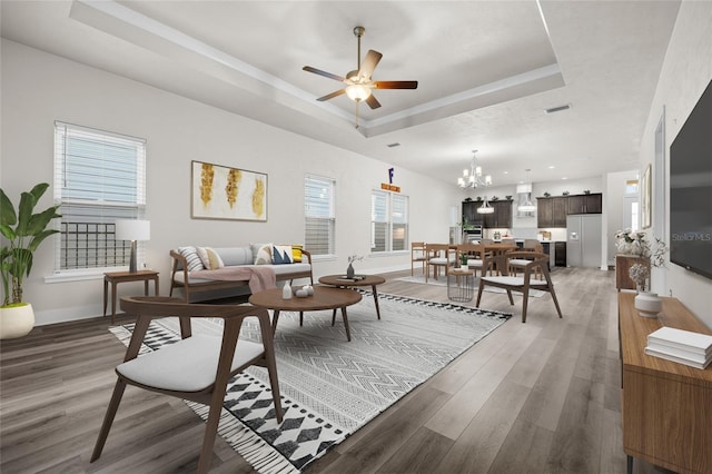 living room featuring ceiling fan with notable chandelier, a tray ceiling, light wood-style floors, and baseboards