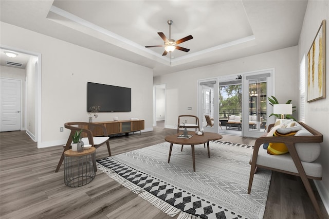 living room with a ceiling fan, a tray ceiling, baseboards, and wood finished floors