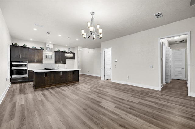kitchen with dark brown cabinetry, stainless steel double oven, open floor plan, wall chimney range hood, and visible vents